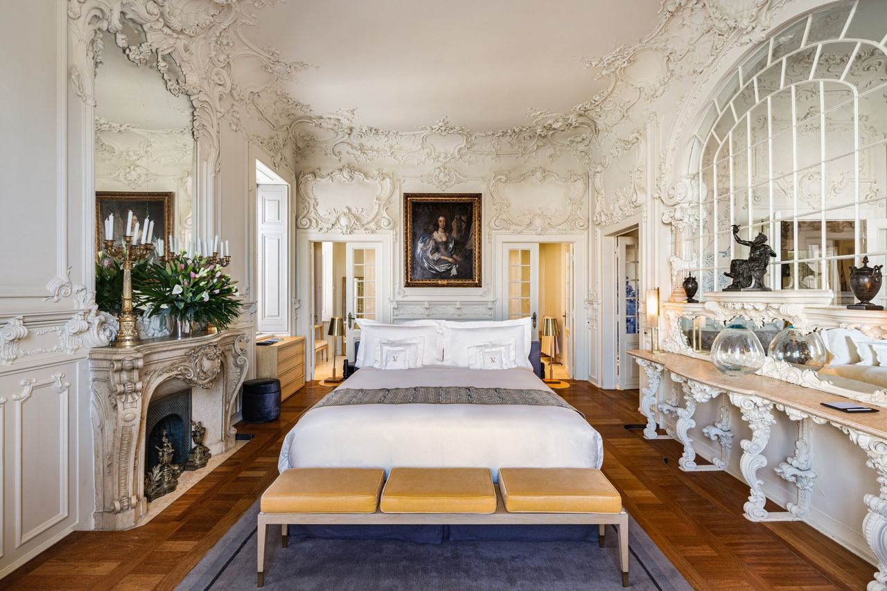 A suite at the Verride Palácio with white rococo stucco, a carved marble fireplace and an arched mirror